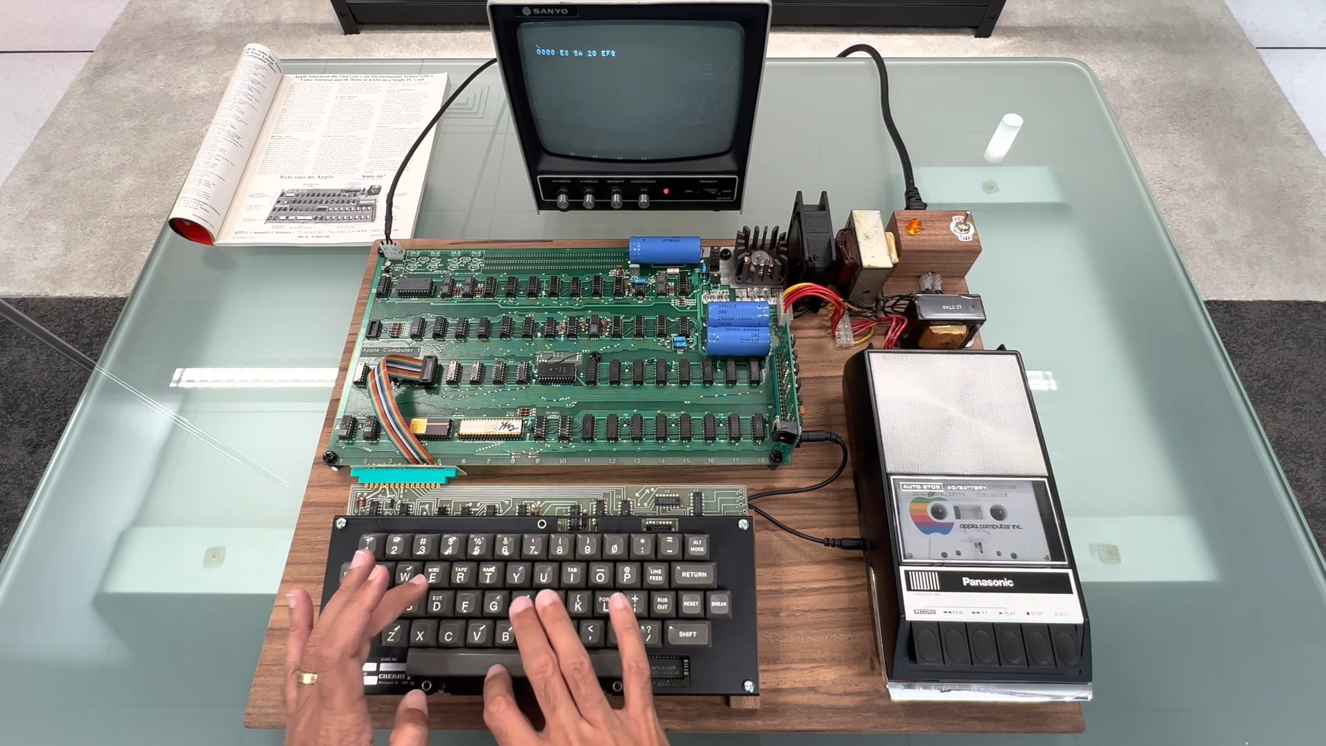 Apple-1 computer, sat on a table, with a person typing on its keyboard.
